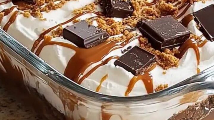 A glass dish filled with layers of whipped cream, caramel, and chocolate cookies, topped with dark chocolate squares.
