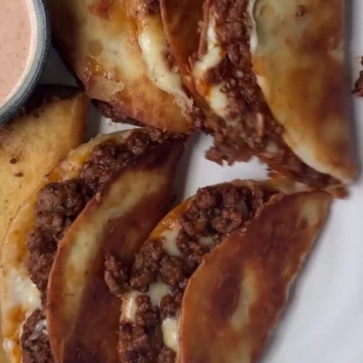 Golden crispy folded beef taco with melted cheese and pico, held by fingers, showing a crunchy bite.