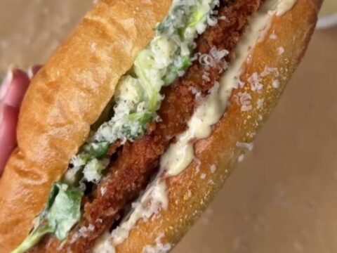 A crispy chicken Caesar sandwich on a buttered brioche bun, with romaine and parmesan peeking out.