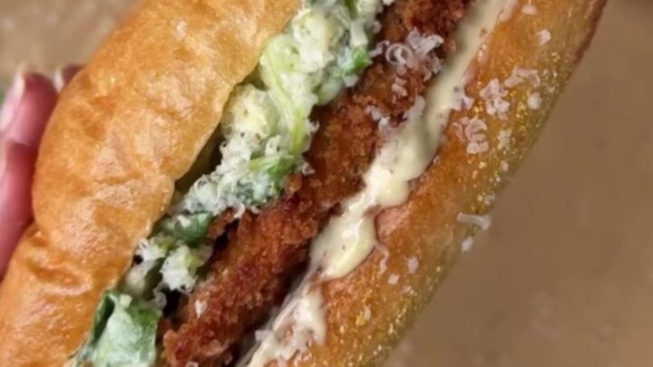 A crispy chicken Caesar sandwich on a buttered brioche bun, with romaine and parmesan peeking out.