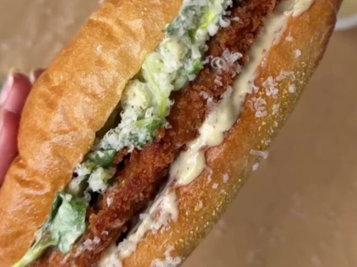 A crispy chicken Caesar sandwich on a buttered brioche bun, with romaine and parmesan peeking out.