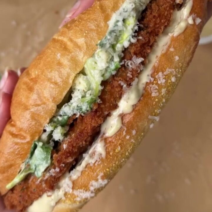A crispy chicken Caesar sandwich on a buttered brioche bun, with romaine and parmesan peeking out.