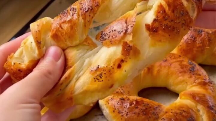 Golden-brown twisted Turkish açma bagels with nigella seeds on a parchment-lined baking sheet