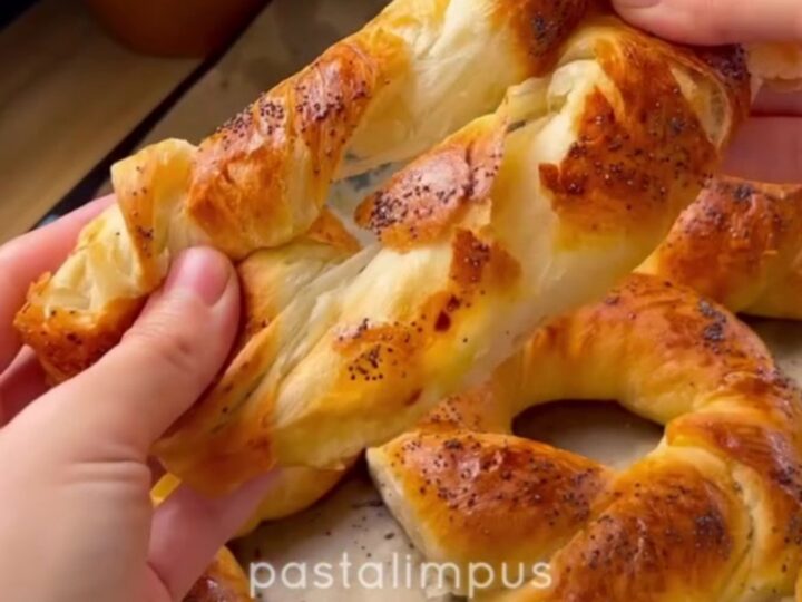 Golden-brown twisted Turkish açma bagels with nigella seeds on a parchment-lined baking sheet