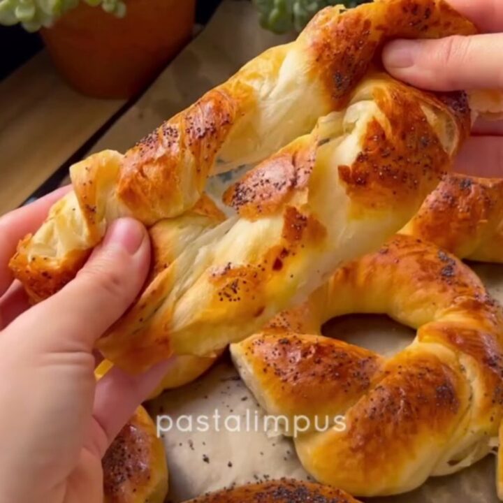 Golden-brown twisted Turkish açma bagels with nigella seeds on a parchment-lined baking sheet
