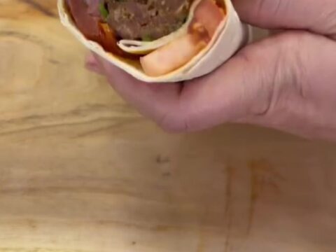 Charred Adana kebab wrap sliced in half, showing juicy meat, sumac onions, and roasted tomatoes in toasted lavash