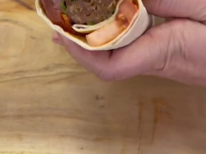 Charred Adana kebab wrap sliced in half, showing juicy meat, sumac onions, and roasted tomatoes in toasted lavash