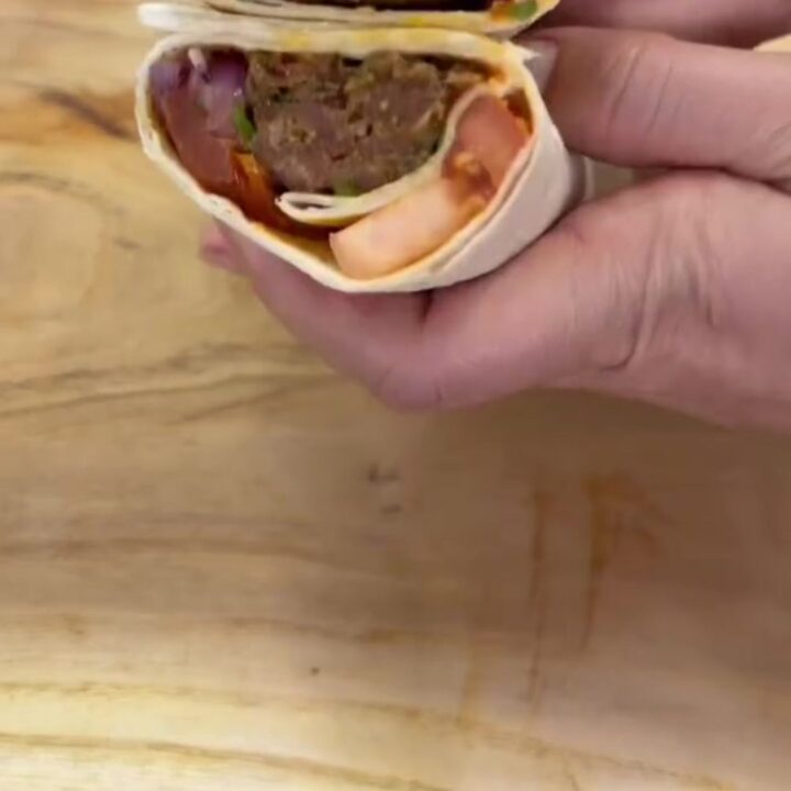 Charred Adana kebab wrap sliced in half, showing juicy meat, sumac onions, and roasted tomatoes in toasted lavash