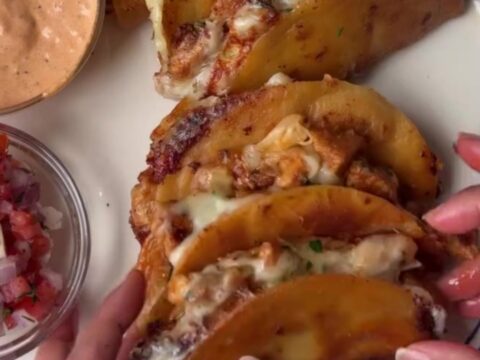 Golden crispy mini tacos stacked on a rustic wooden board with a bowl of lime crema
