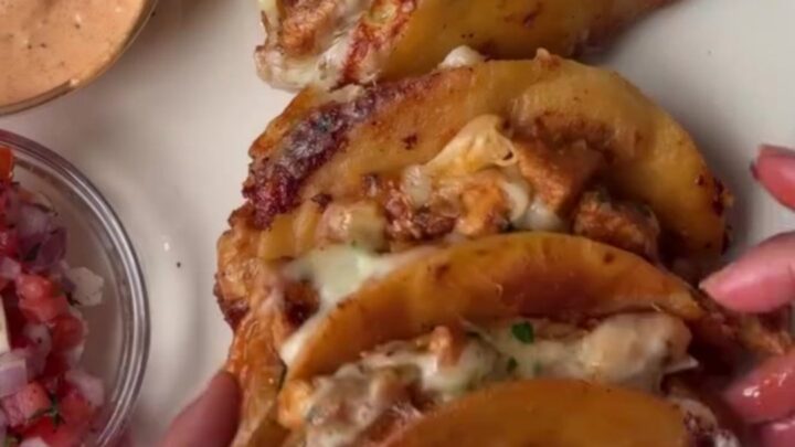 Golden crispy mini tacos stacked on a rustic wooden board with a bowl of lime crema
