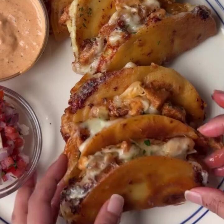 Golden crispy mini tacos stacked on a rustic wooden board with a bowl of lime crema