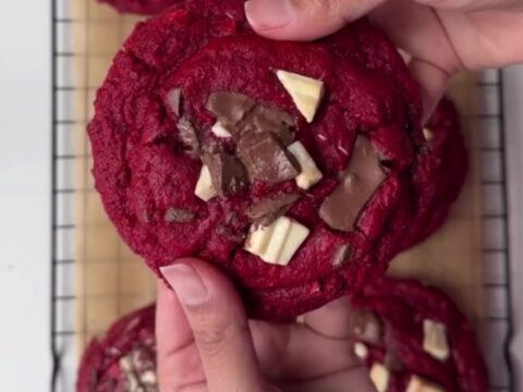 Giant red velvet cookies with melted chocolate chunks, stacked on a plate.
