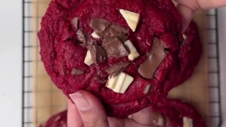 Giant red velvet cookies with melted chocolate chunks, stacked on a plate.