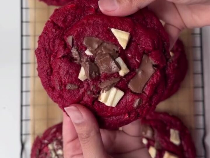 Giant red velvet cookies with melted chocolate chunks, stacked on a plate.