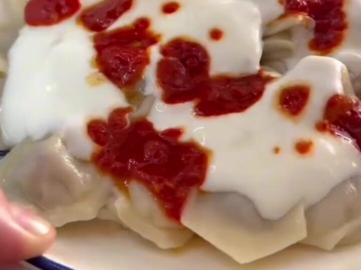 A bowl of Turkish manti dumplings topped with garlic yogurt and sizzling red paprika butter.