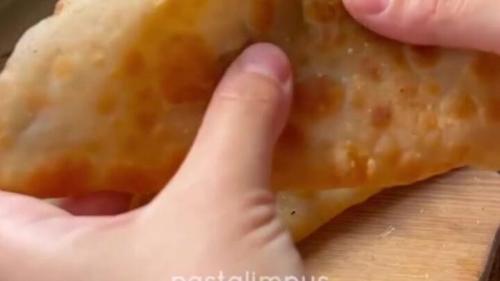 Golden puffed çi börek on a wire rack, blistered crust, steam rising, savory meat filling visible.