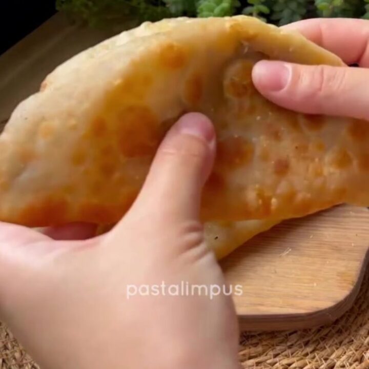 Golden puffed çi börek on a wire rack, blistered crust, steam rising, savory meat filling visible.