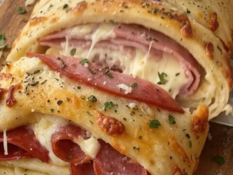 A golden-brown ham and pepperoni stromboli sliced on a wooden board with melted cheese visible.