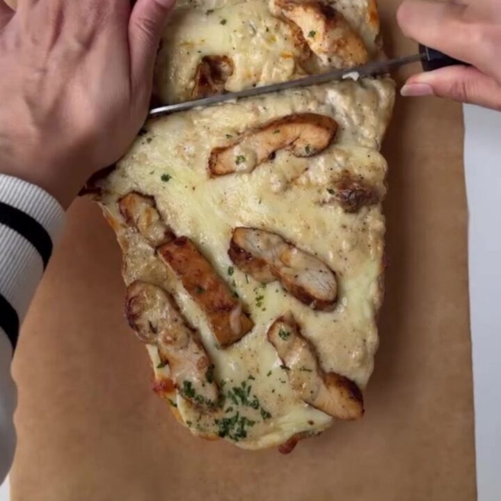 Cheesy chicken Alfredo stuffed garlic bread on a baking sheet, with melted mozzarella and golden crust.