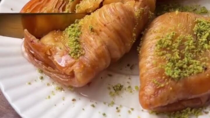 Golden crispy mussel-shaped baklava on a tray with lemon syrup being poured over