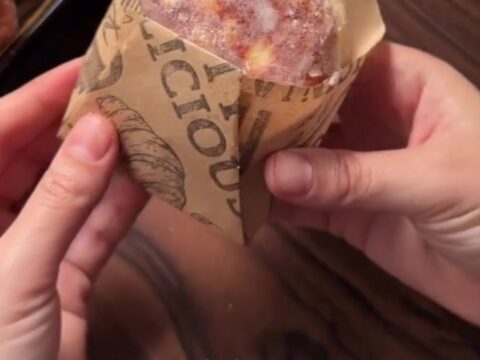 A sugar-coated donut with chocolate hazelnut filling oozing out, held in a parchment paper cone.