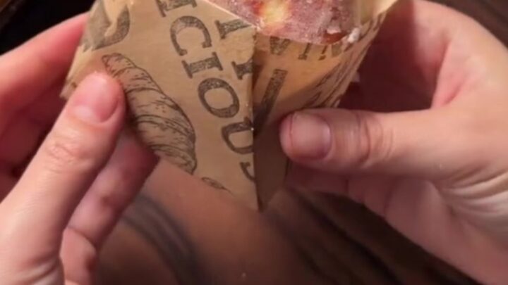 A sugar-coated donut with chocolate hazelnut filling oozing out, held in a parchment paper cone.