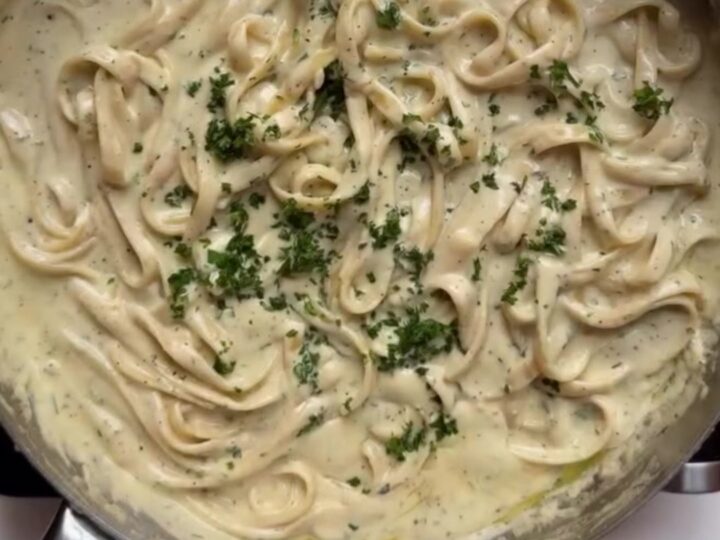 A fork twirls creamy fettuccine Alfredo with parmesan and parsley