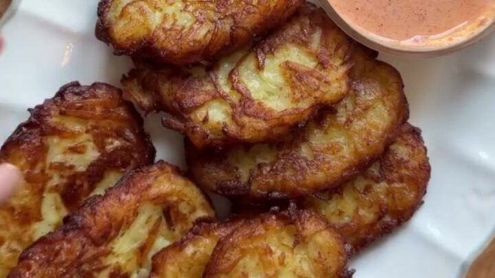 Golden crispy garlic parmesan hashbrowns stacked on a plate with a fork breaking one open