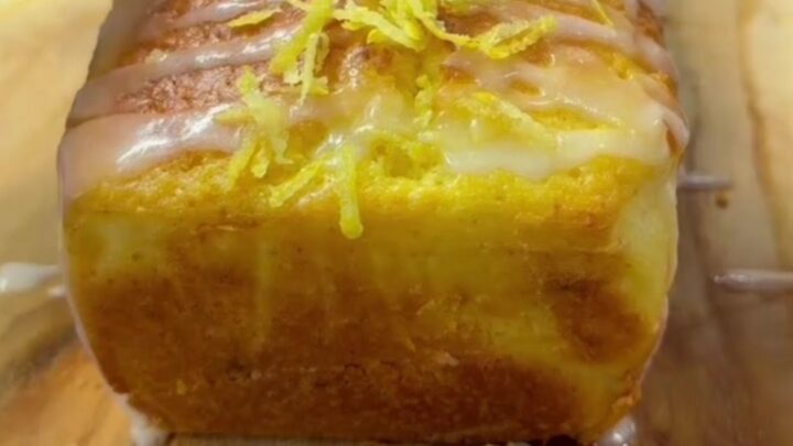 Whole lemon walnut loaf cake with glossy glaze on a wooden board