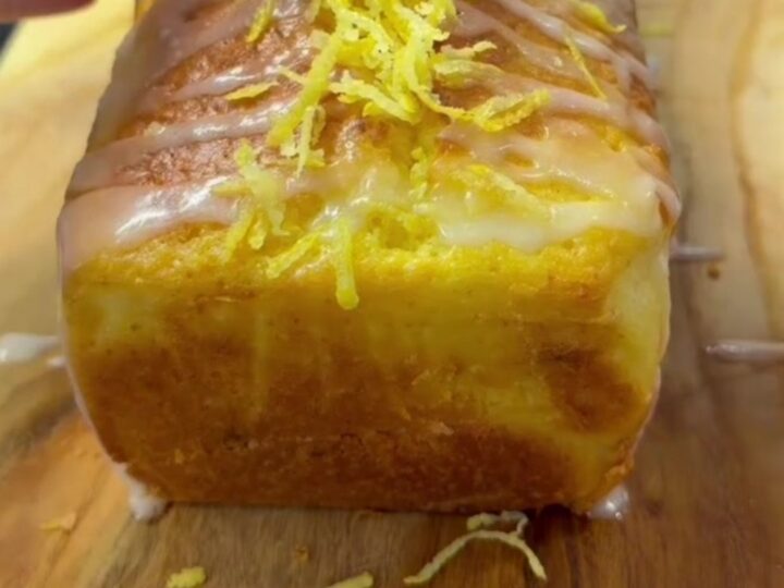 Whole lemon walnut loaf cake with glossy glaze on a wooden board