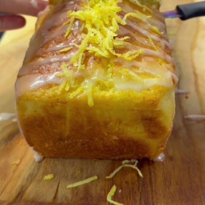 Whole lemon walnut loaf cake with glossy glaze on a wooden board