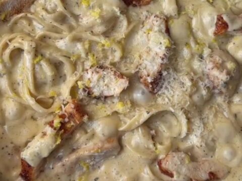 A fork twirling fettuccine in a creamy lemon garlic sauce with slices of seared chicken breast on top.