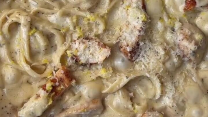 A fork twirling fettuccine in a creamy lemon garlic sauce with slices of seared chicken breast on top.