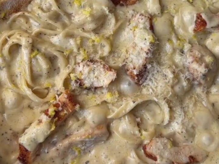 A fork twirling fettuccine in a creamy lemon garlic sauce with slices of seared chicken breast on top.