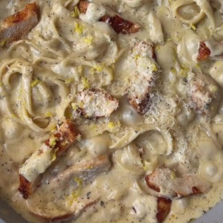 A fork twirling fettuccine in a creamy lemon garlic sauce with slices of seared chicken breast on top.