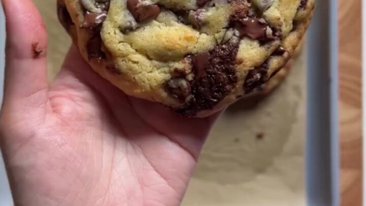 Hands pulling apart a giant golden cookie with molten chocolate stretching