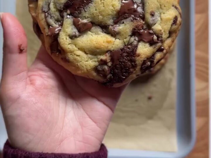 Hands pulling apart a giant golden cookie with molten chocolate stretching