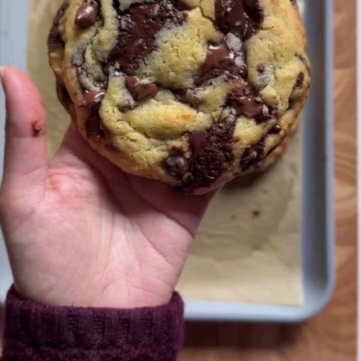 Hands pulling apart a giant golden cookie with molten chocolate stretching
