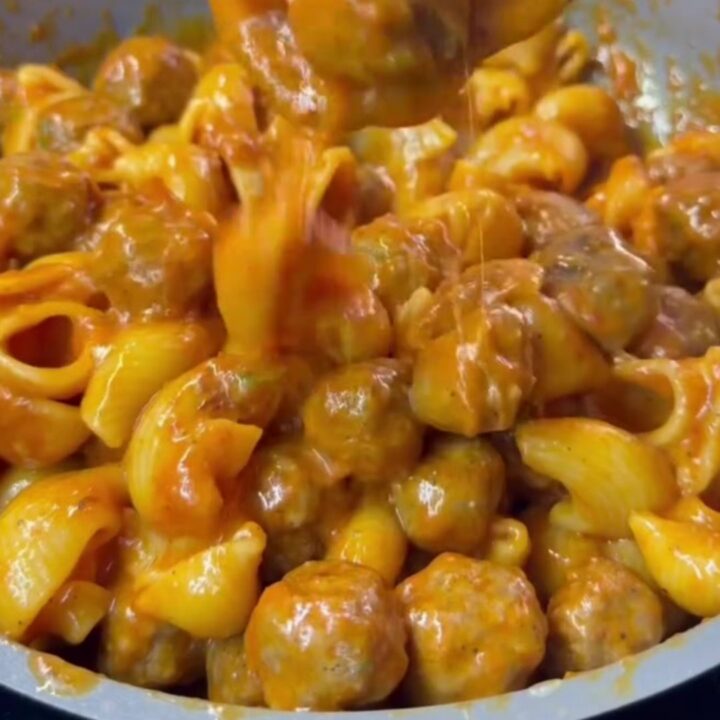 Skillet of rigatoni with melted mozzarella and basil, cheese pulling from the spoon