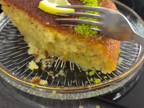 Golden Revani cake with lemon syrup, topped with crushed pistachios and shredded coconut, on a serving plate.