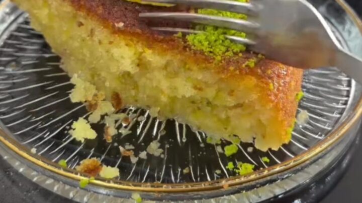 Golden Revani cake with lemon syrup, topped with crushed pistachios and shredded coconut, on a serving plate.