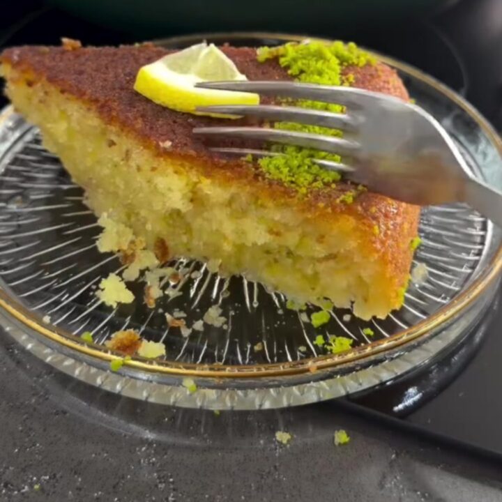 Golden Revani cake with lemon syrup, topped with crushed pistachios and shredded coconut, on a serving plate.