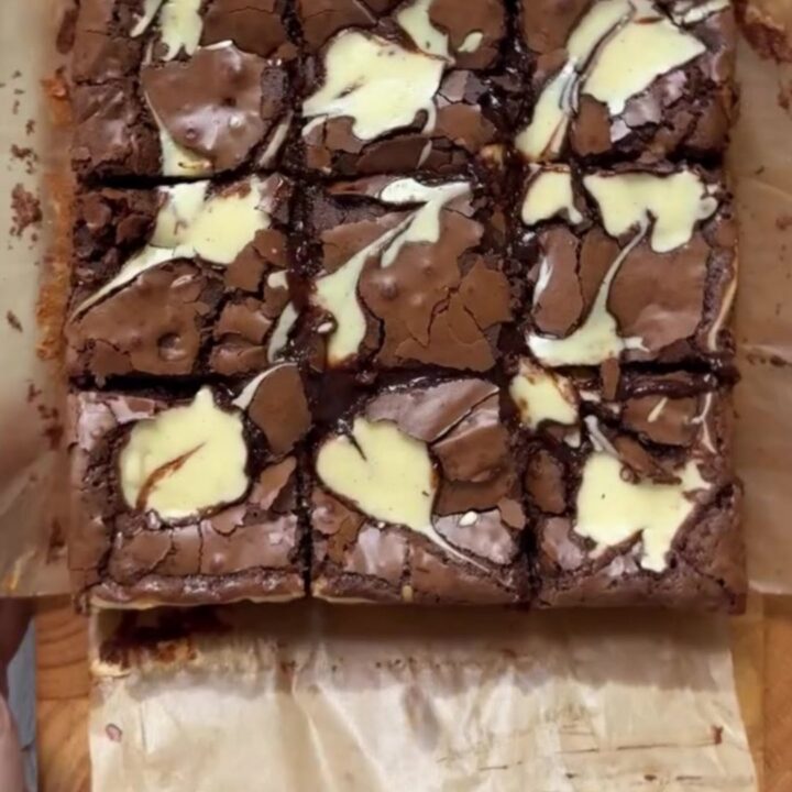 A stack of fudgy brown butter cheesecake brownies with visible swirls on a plate.