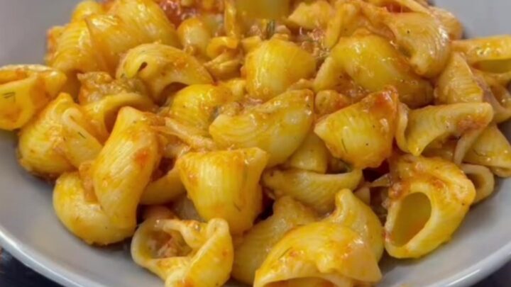 A skillet filled with shell pasta in creamy roasted tomato and pepper sauce, topped with fresh basil and black pepper.