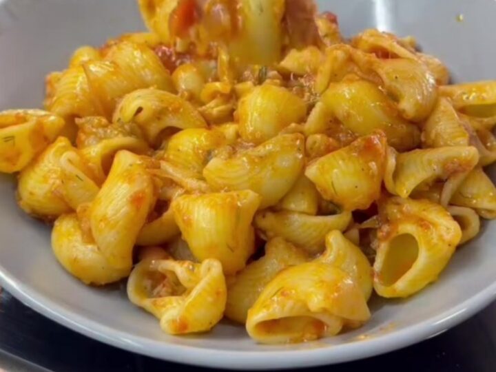 A skillet filled with shell pasta in creamy roasted tomato and pepper sauce, topped with fresh basil and black pepper.