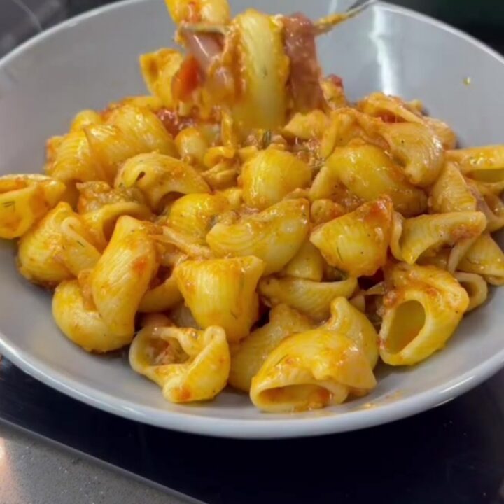 A skillet filled with shell pasta in creamy roasted tomato and pepper sauce, topped with fresh basil and black pepper.