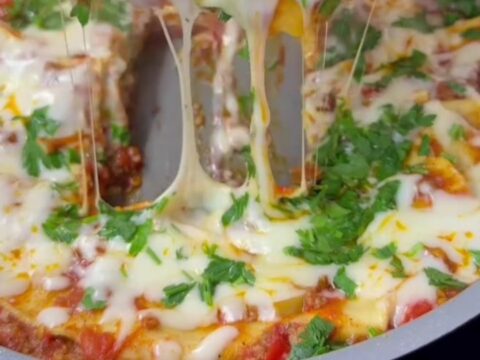 Lasagna rollups standing upright in a skillet, topped with melted mozzarella and fresh basil.