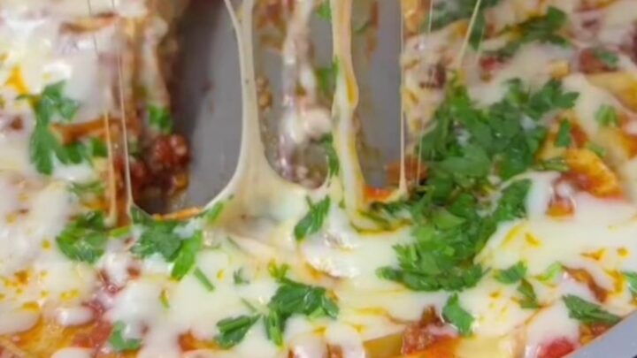 Lasagna rollups standing upright in a skillet, topped with melted mozzarella and fresh basil.