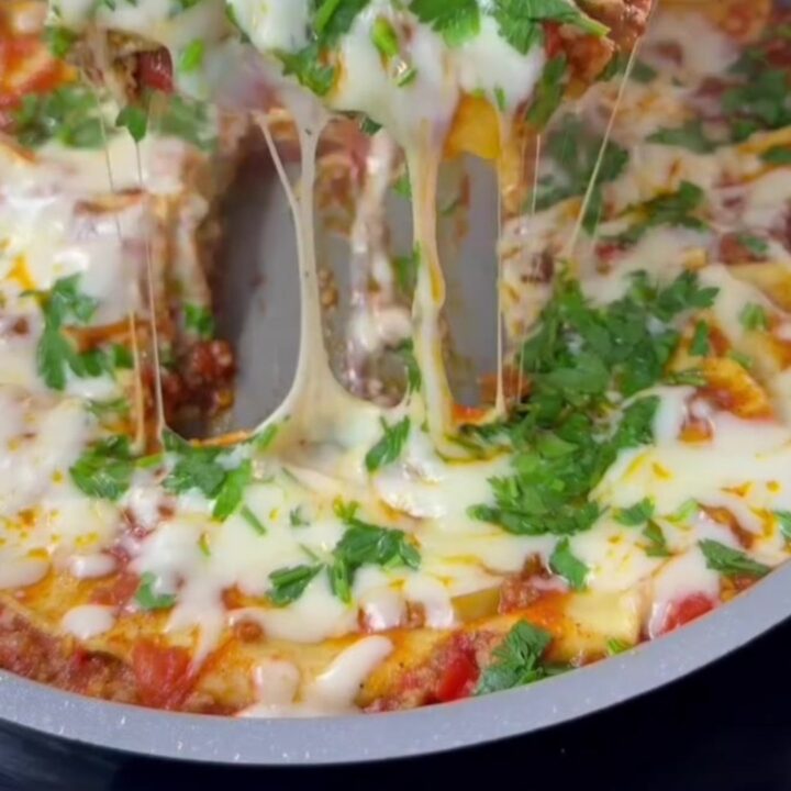 Lasagna rollups standing upright in a skillet, topped with melted mozzarella and fresh basil.