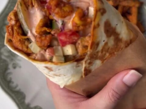 Crispy chicken shawarma wrap cut in half, showing layers of chicken, fries, and pickled turnips, with garlic sauce.